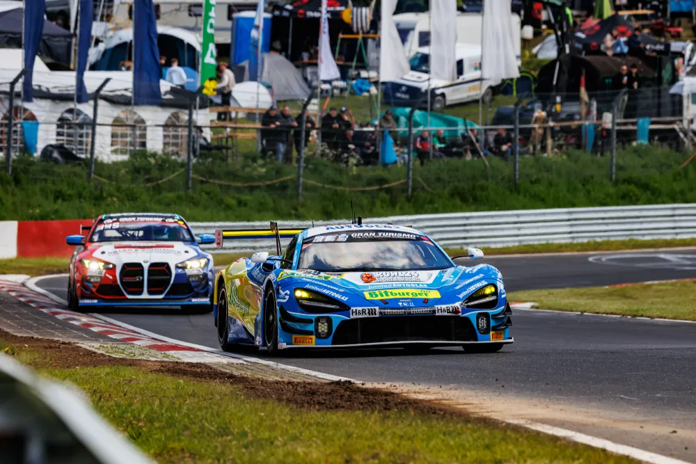 Blauer McLaren 720S GT3 vor einem BMW M4 in der Kurve, Zuschauer am Streckenrand