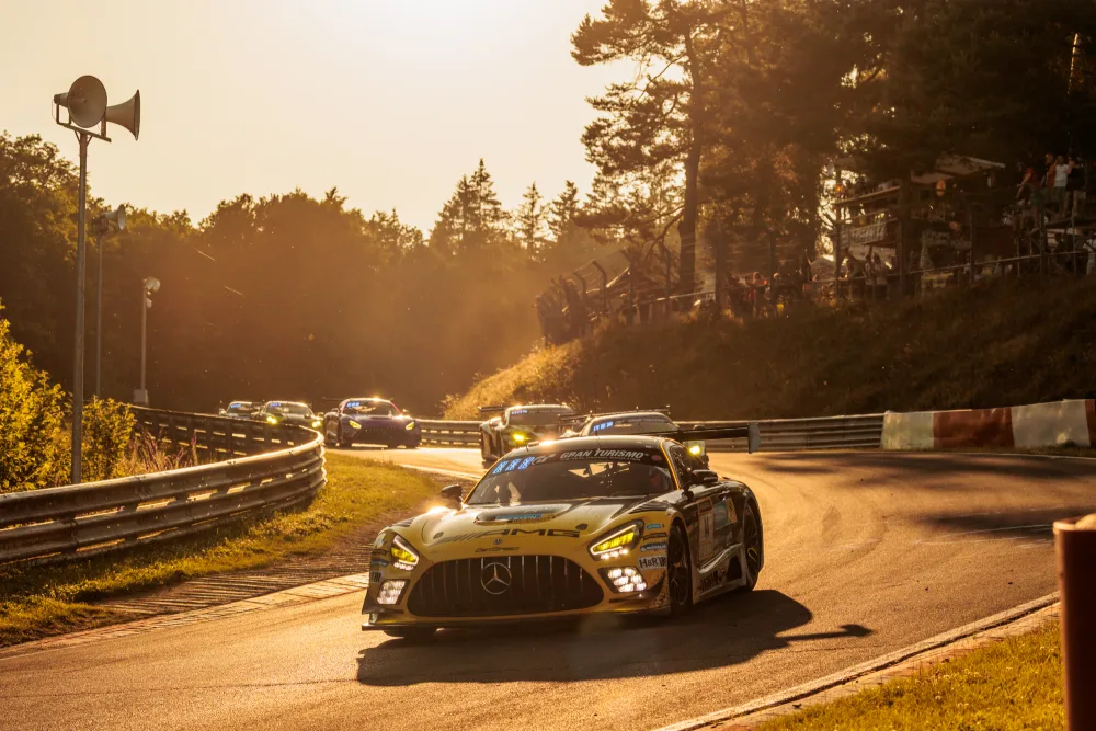 Mercedes-AMG GT3 im Gegenlicht der Abendsonne, weiteres Fahrzeugfeld in der Kurve dahinter