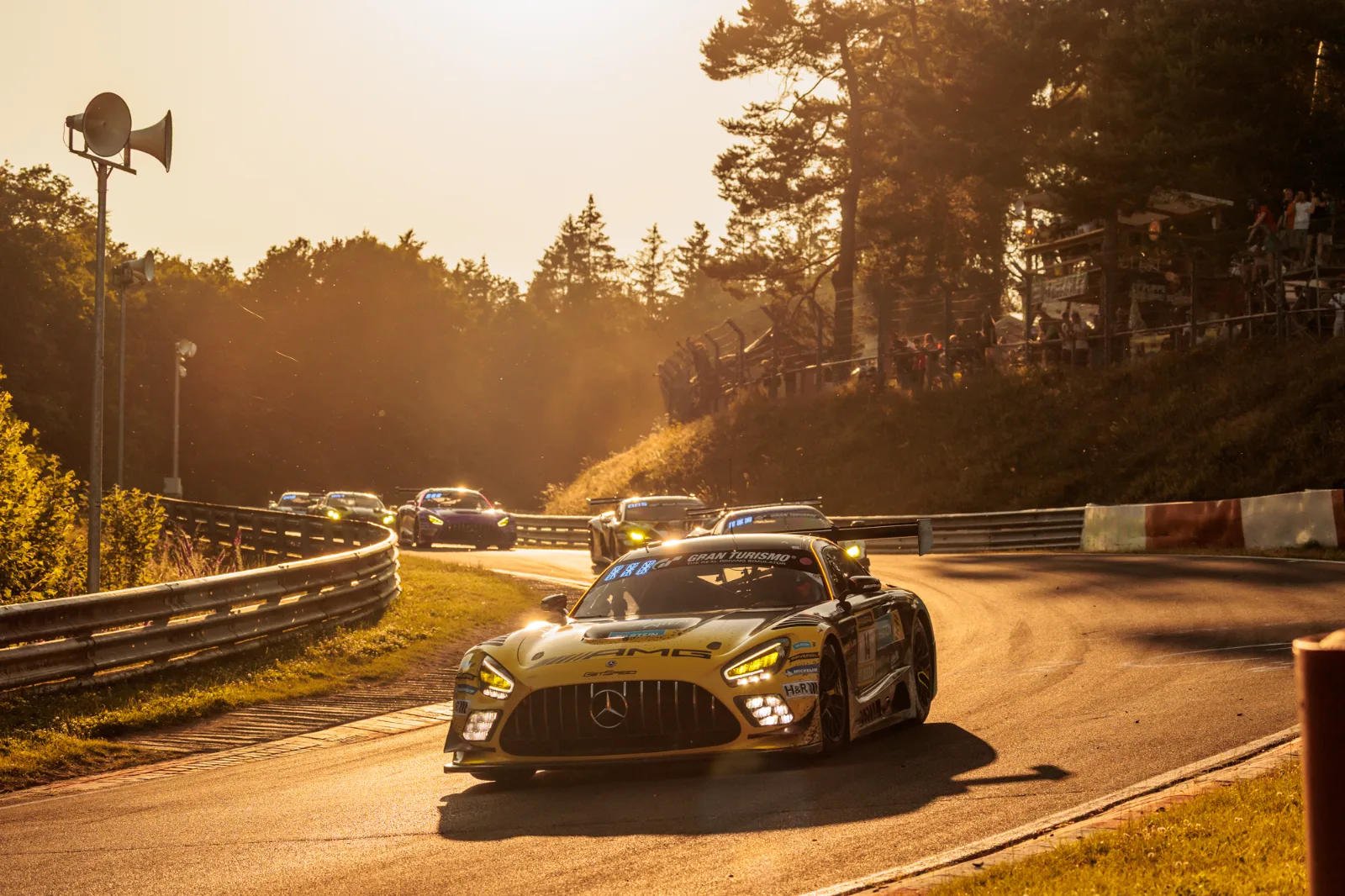 Mercedes-AMG GT3 im Gegenlicht der Abendsonne, weiteres Fahrzeugfeld in der Kurve dahinter