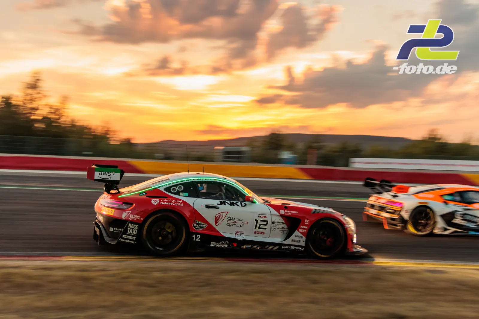 BMW M4 GT3 im Mitzieher bei Sonnenuntergang während der 24 Stunden von Spa-Francorchamps, dramatischer Himmel im Hintergrund.