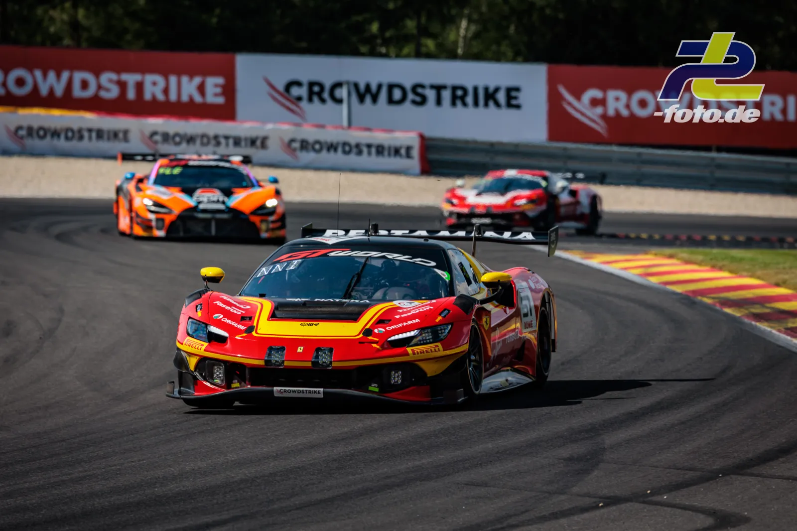 Ferrari 296 GT3 EVO von AF Corse in rot-gelber Lackierung auf der Rennstrecke in Spa-Francorchamps, gefolgt von Konkurrenzfahrzeugen.