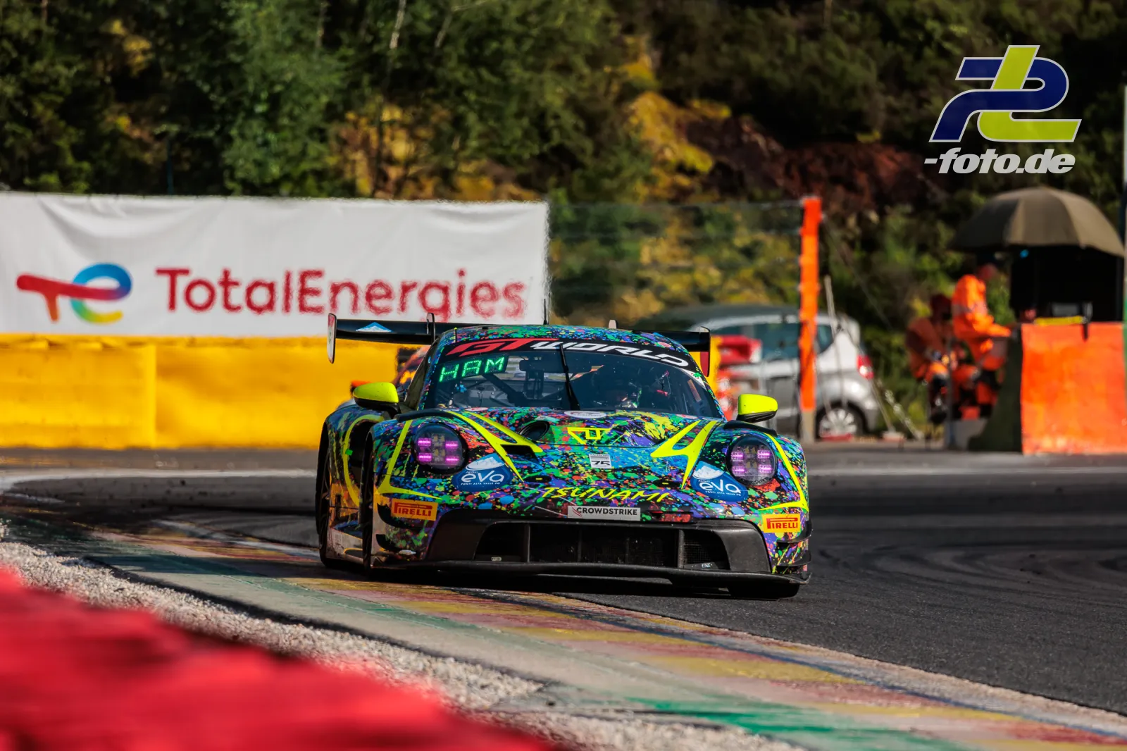 Porsche 911 GT3 R mit neonbunter Lackierung auf der Strecke beim 24h-Rennen von Spa-Francorchamps, Randsteine im Vordergrund.