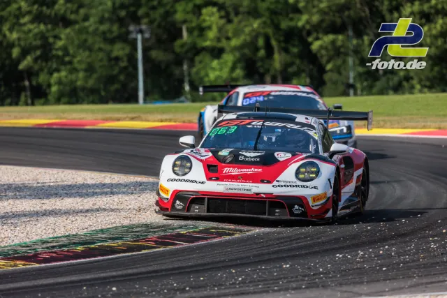 Rennwagen fährt über Randstein in Spa-Francorchamps beim 24-Stunden-Rennen, gefolgt von Konkurrenten. Kiesbett und Wald im Hintergrund.