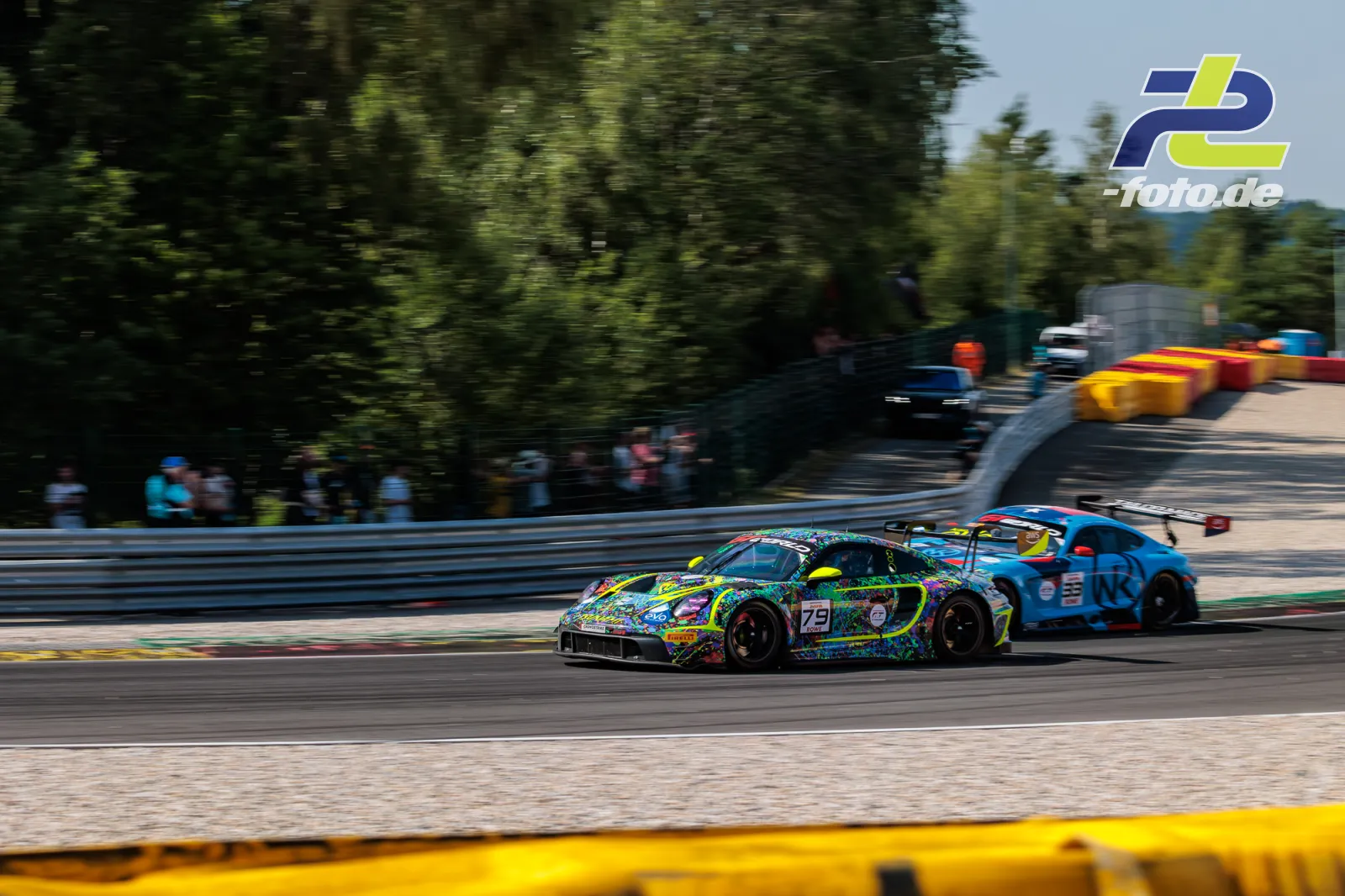 Porsche 911 GT3 R mit bunter Lackierung auf der Strecke in Spa-Francorchamps beim 24-Stunden-Rennen, gefolgt von einem blauen Fahrzeug.