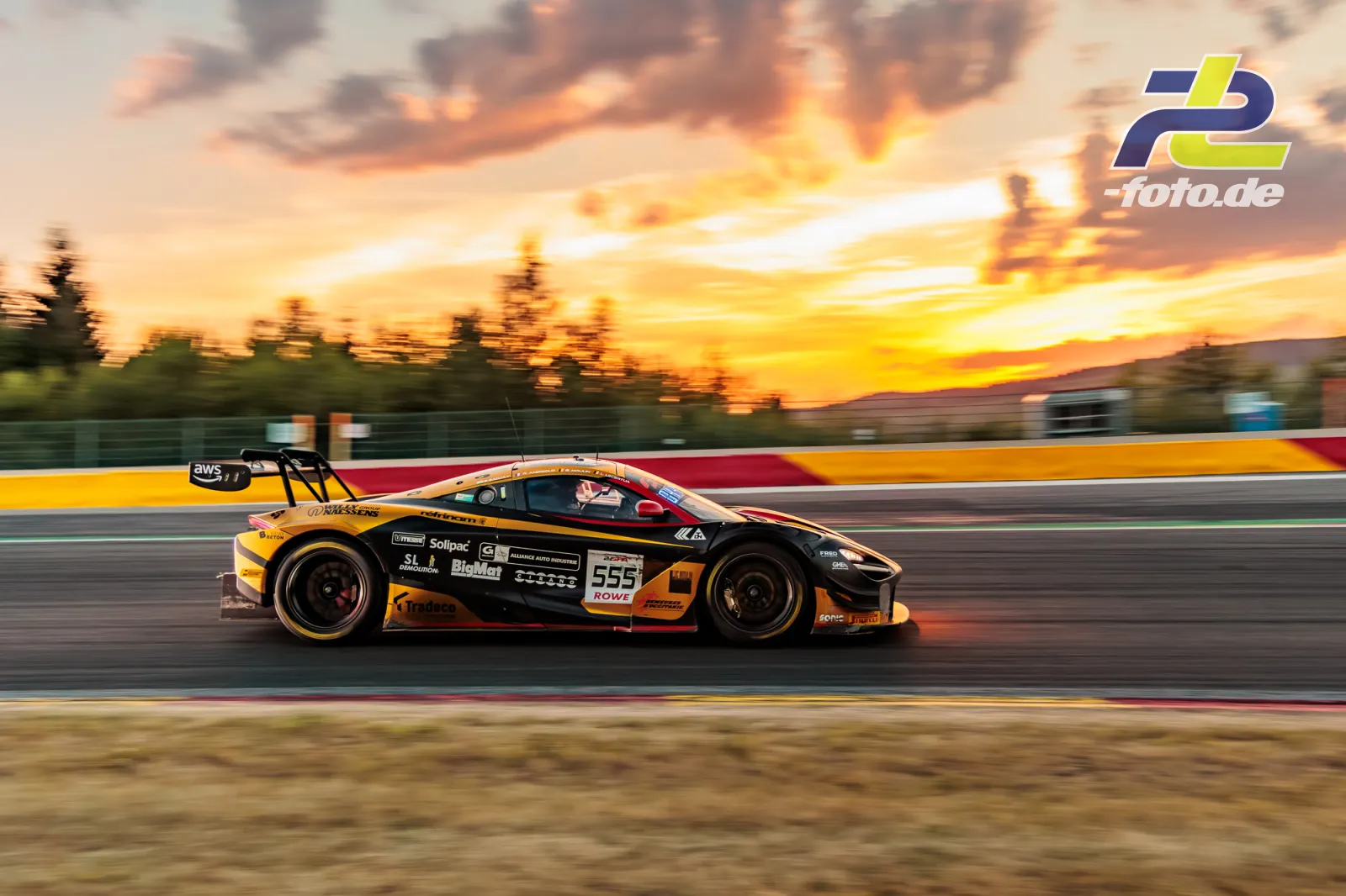 Porsche 718 Cayman GT4 #555 im Abendlicht beim 24-Stunden-Rennen von Spa-Francorchamps, Seitenansicht mit Sonnenuntergang im Hintergrund.