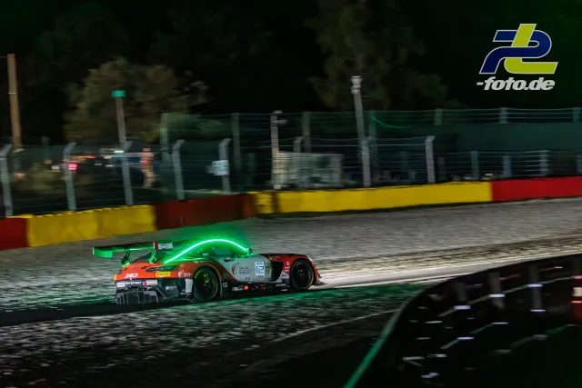 Porsche 911 GT3 R #12 bei Nacht auf dem Kurs in Spa-Francorchamps während des 24-Stunden-Rennens, Kurvenausgang mit grüner Beleuchtung.