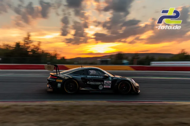 Porsche 911 GT3 R im Mitzieher bei Sonnenuntergang während der 24 Stunden von Spa-Francorchamps, dramatischer Himmel mit goldenen Wolken.