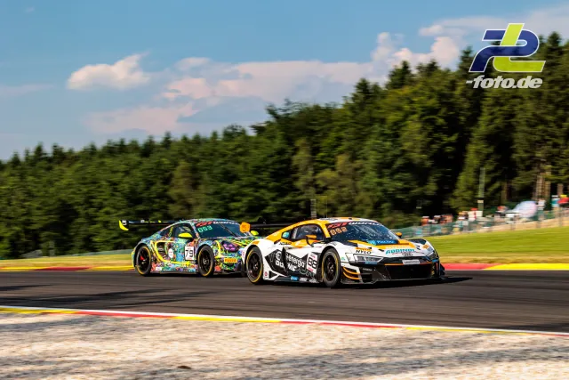 Zwei GT3-Fahrzeuge im Rennduell beim 24h-Rennen Spa-Francorchamps, Audi R8 vorne, bunter Porsche dahinter, über Randstein fahrend.