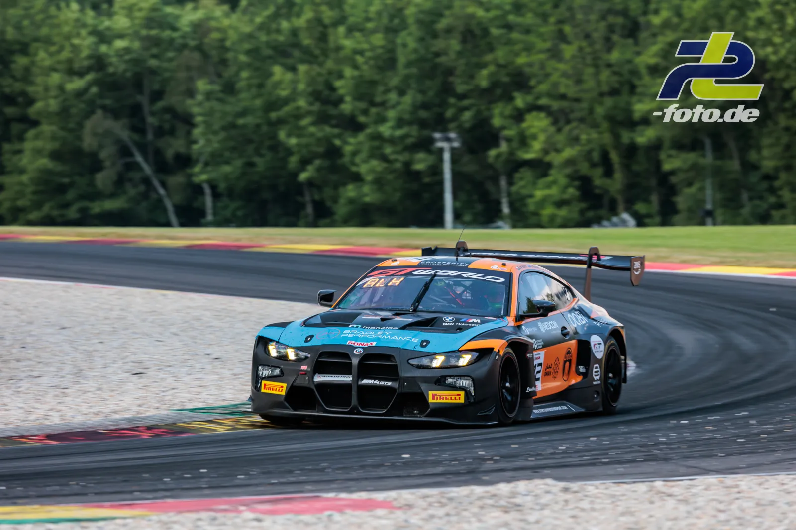 BMW M4 GT3 EVO in der Kurve beim 24-Stunden-Rennen von Spa-Francorchamps, türkis-orange Lackierung, Randsteine im Hintergrund