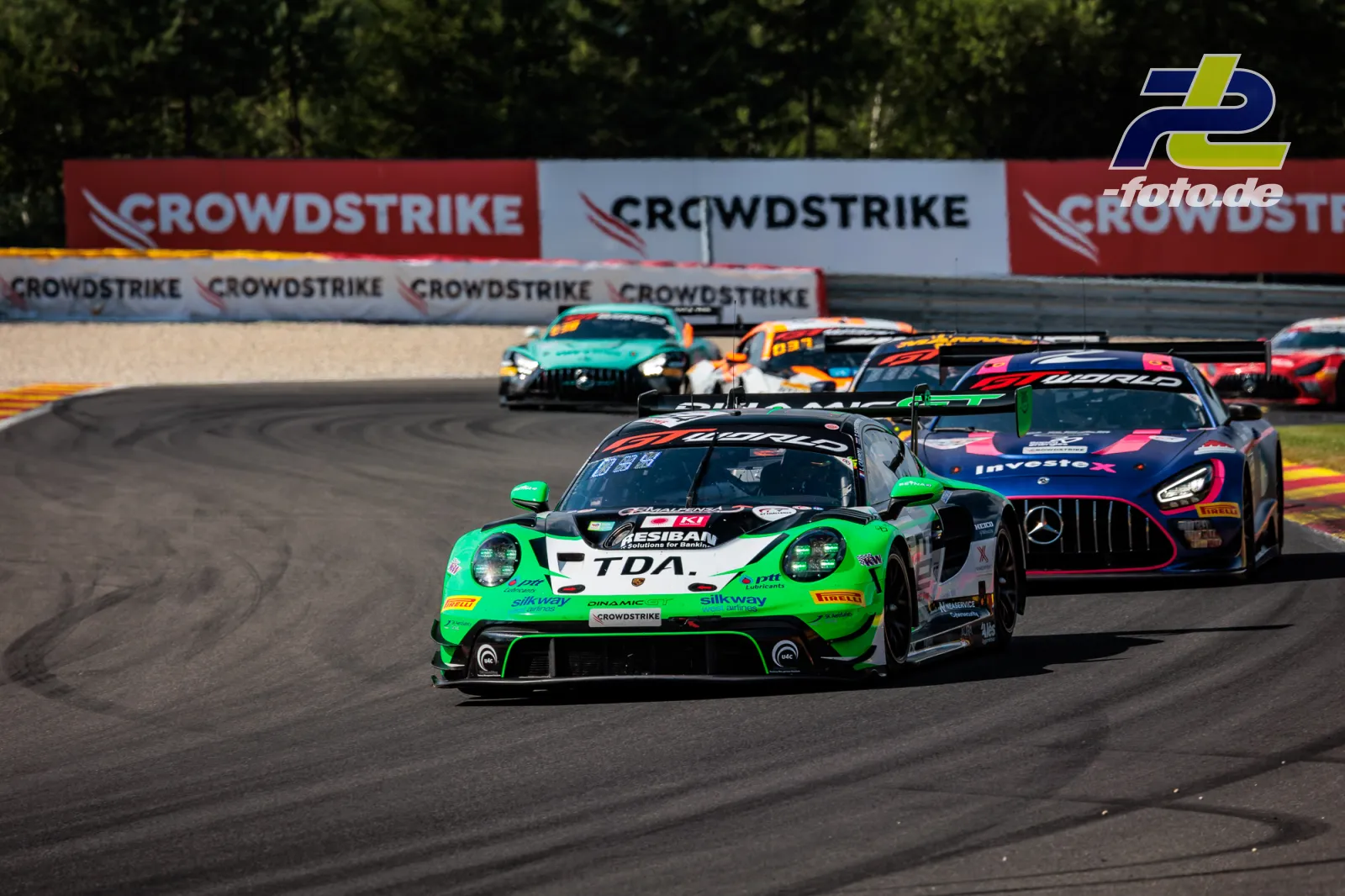Grüner Porsche 911 GT3 R führt Fahrzeugfeld durch eine Kurve beim 24-Stunden-Rennen von Spa-Francorchamps.