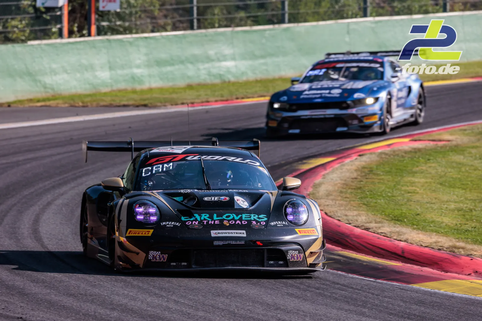 Porsche 911 GT3 R in Kurve bei den 24h von Spa-Francorchamps, gefolgt von einem weiteren GT3-Fahrzeug über rot-gelben Randsteinen.