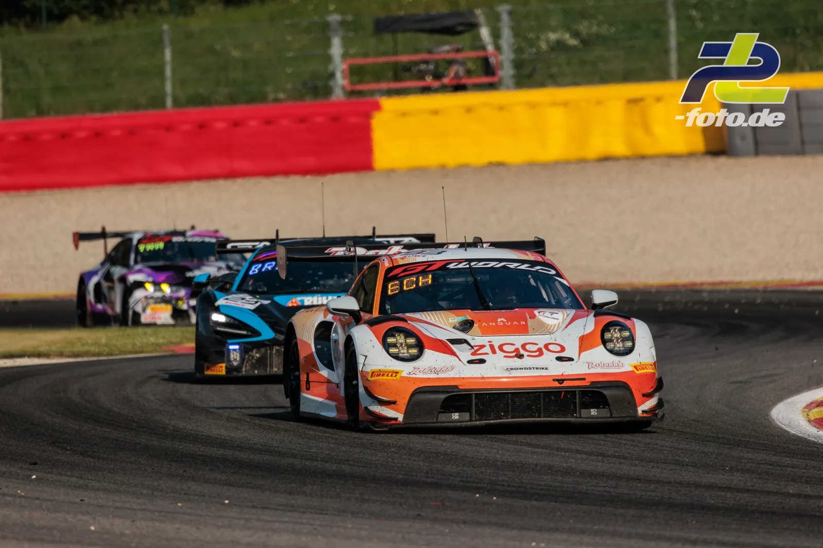 Porsche 911 GT3 R in orange-weiß führt eine Gruppe von GT-Fahrzeugen durch eine Kurve beim 24-Stunden-Rennen von Spa-Francorchamps.
