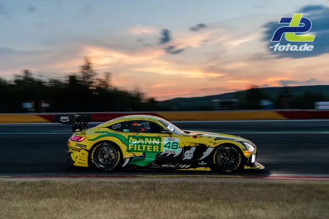 BMW M4 GT3 Nummer 48 in gelb-grüner Lackierung bei Abenddämmerung auf der Rennstrecke von Spa-Francorchamps während des 24-Stunden-Rennens.