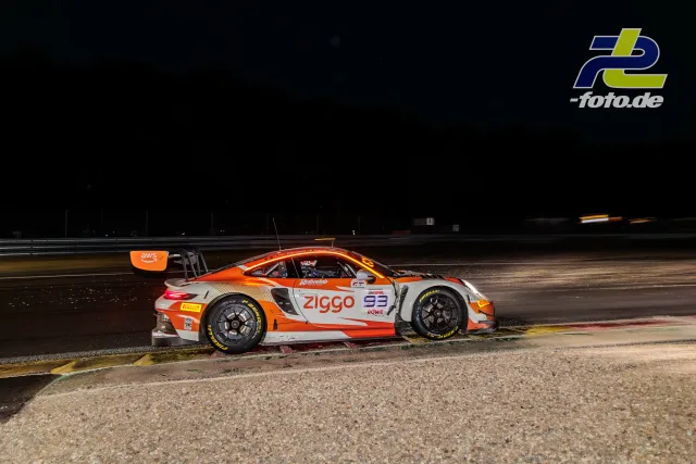 Porsche 911 GT3 R bei Nacht auf der Strecke in Spa-Francorchamps, Seitenansicht mit orange-weißer Lackierung am Kurvenrand.