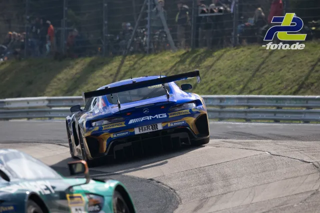 Mercedes-AMG GT3 in blau-gold auf der Nordschleife, verfolgt von einem Audi R8 LMS, Zuschauer am Streckenrand