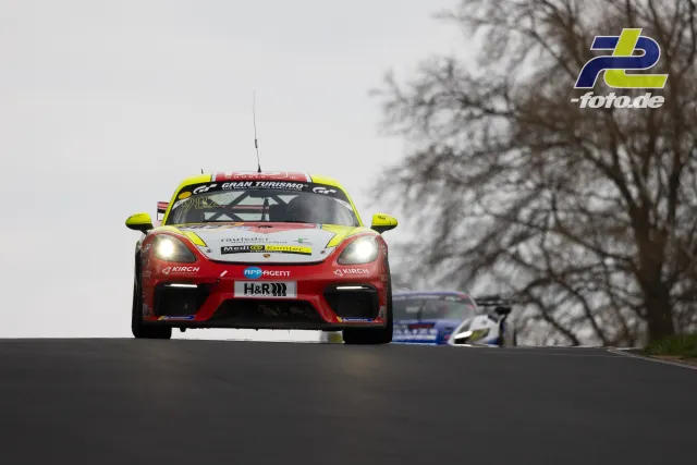 Porsche 718 Cayman GT4 mit Startnummer 982 in roter, gelber und weißer Lackierung über eine Kuppe springend am Nürburgring Nordschleife.