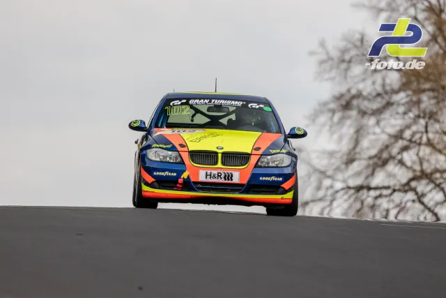 BMW Rennwagen mit Startnummer 102 in bunter Lackierung frontal auf der Bergkuppe der Nordschleife