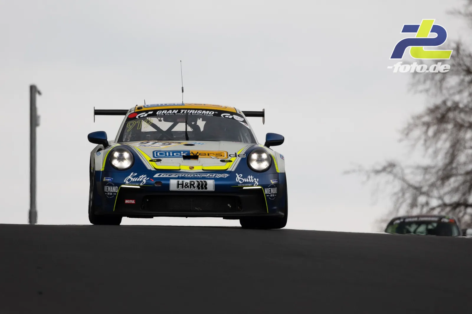 Porsche 911 GT3 Cup springt über eine Bergkuppe auf dem Nürburgring Nordschleife bei bewölktem Himmel während des NLS-Rennens.