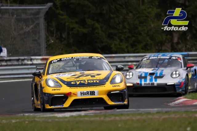 Gelber Porsche 718 Cayman GT4 #352 führt zwei weiße Porsche 911 GT3 durch eine Kurve beim NLS-Rennen am Nürburgring.