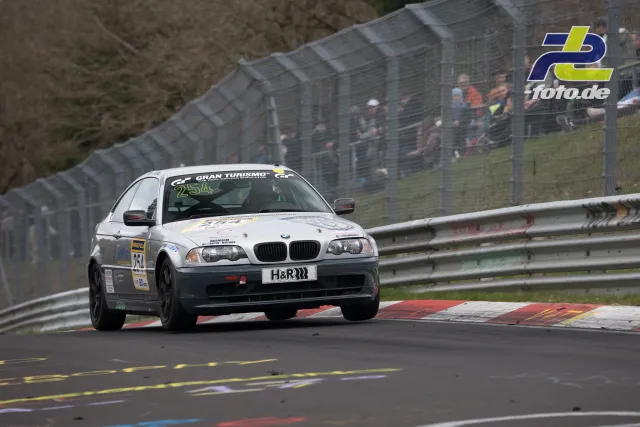 BMW E46 Nummer 254 auf der Nürburgring-Nordschleife, im Hintergrund Fangzaun und Zuschauer beim NLS-Rennen.