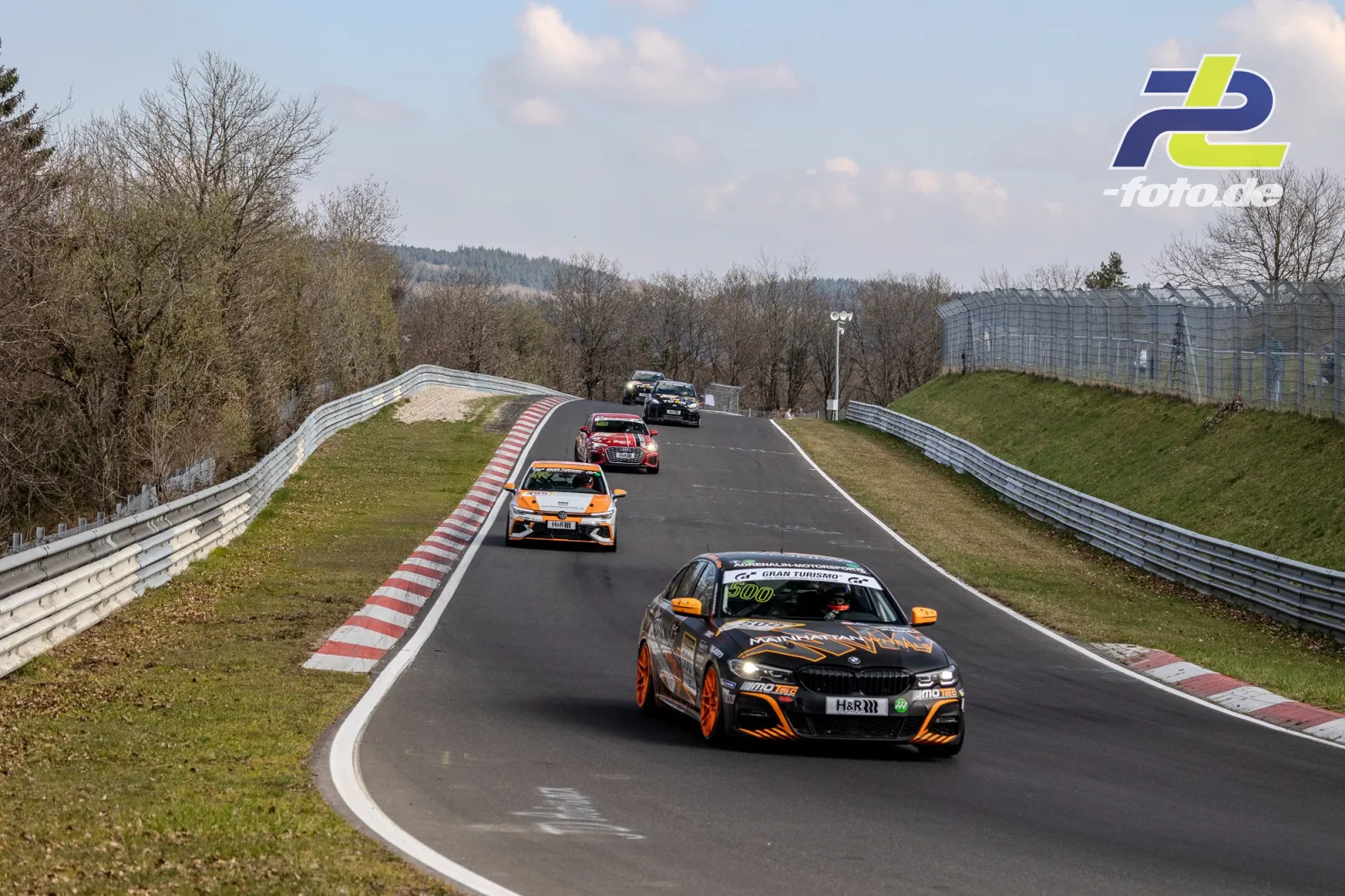 Fünf Fahrzeuge in einer Kuppe auf der Nürburgring-Nordschleife, angeführt von einem schwarz-orangen BMW.