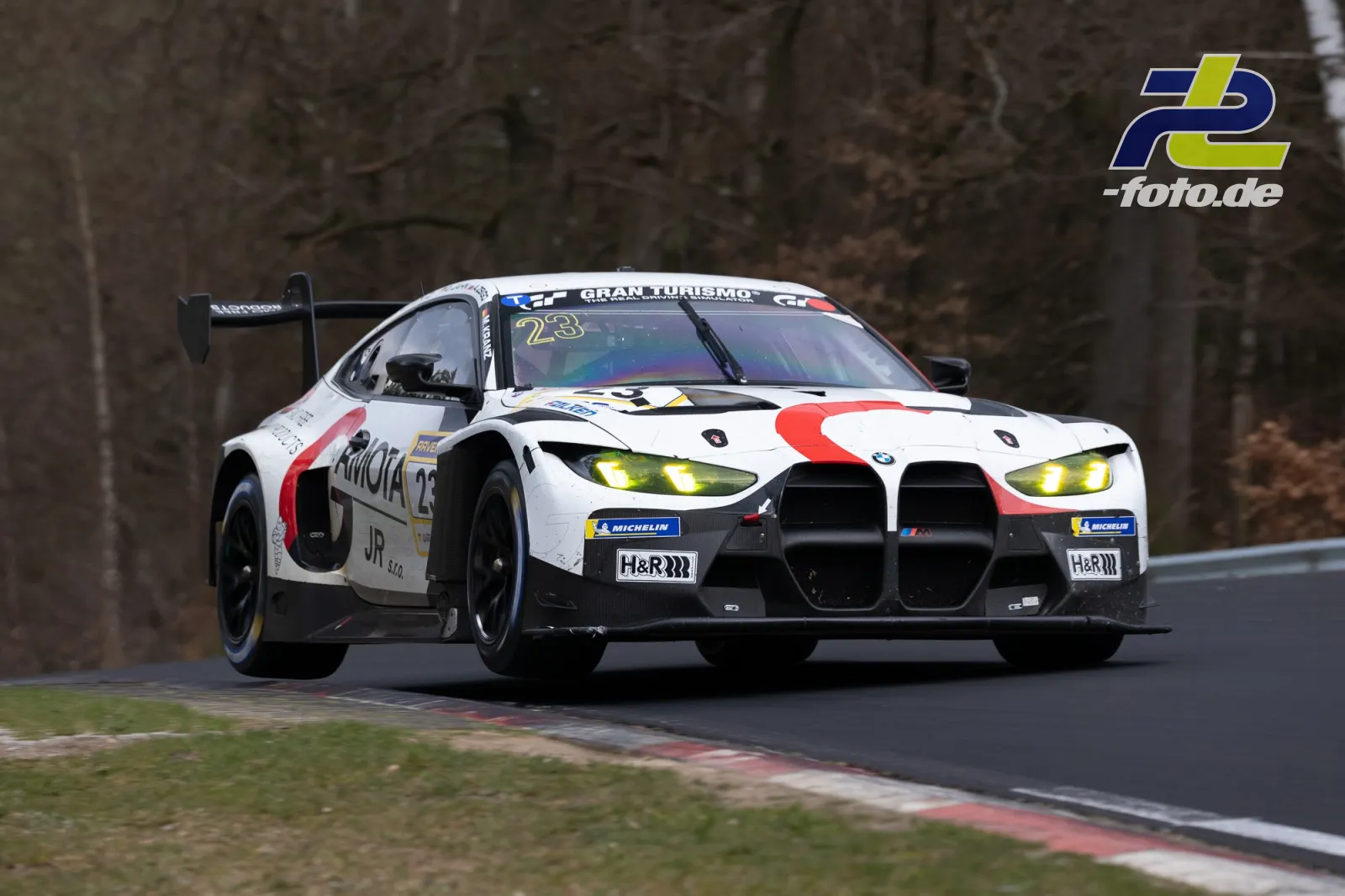 BMW M4 GT3 #23 mit weißer Lackierung und gelben Scheinwerfern auf der Nordschleife des Nürburgrings während des Rennens.