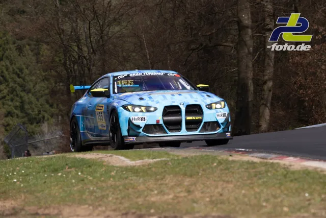 BMW M4 GT4 #155 in Hellblau auf der Nürburgring-Nordschleife, umgeben von Wald bei Tageslicht während des NLS-Rennens.