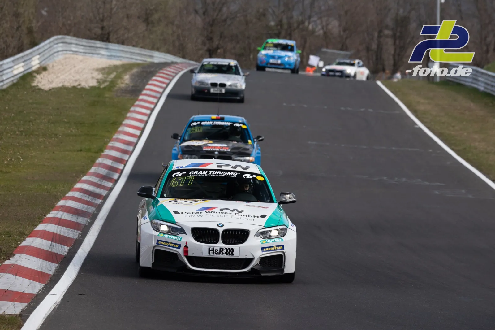Rennszene auf der Nordschleife mit mehreren Fahrzeugen, angeführt von einem weißen BMW mit türkisfarbenen Akzenten