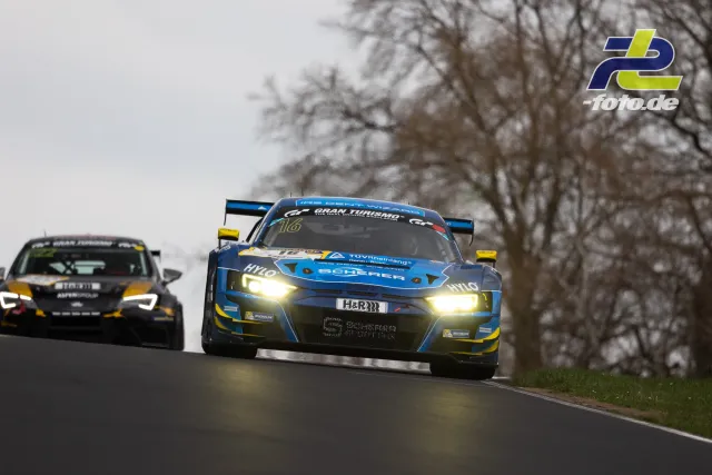 Zwei Rennwagen mit eingeschaltetem Licht fahren bei trüben Bedingungen über die Nordschleife des Nürburgrings.