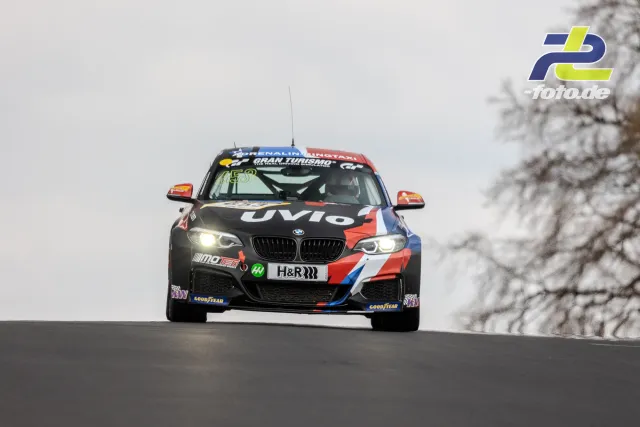 BMW M240i Racing in Frontalansicht auf Kuppe des Nürburgrings bei bewölktem Wetter mit eingeschalteten Scheinwerfern