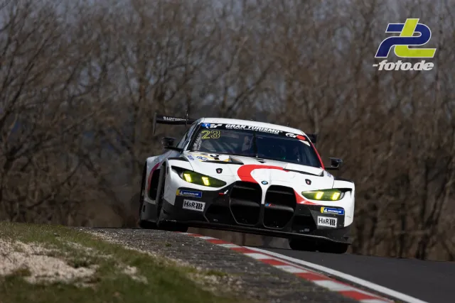 BMW M4 GT3 mit Startnummer 23 über Kuppe am Nürburgring bei bewölktem Wetter während des Rennens.