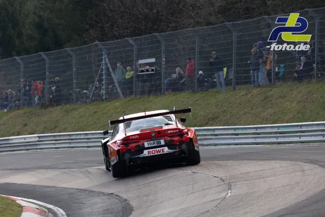 BMW M4 GT3 in rot-weißer Lackierung auf der Nordschleife, Zuschauer am Streckenzaun