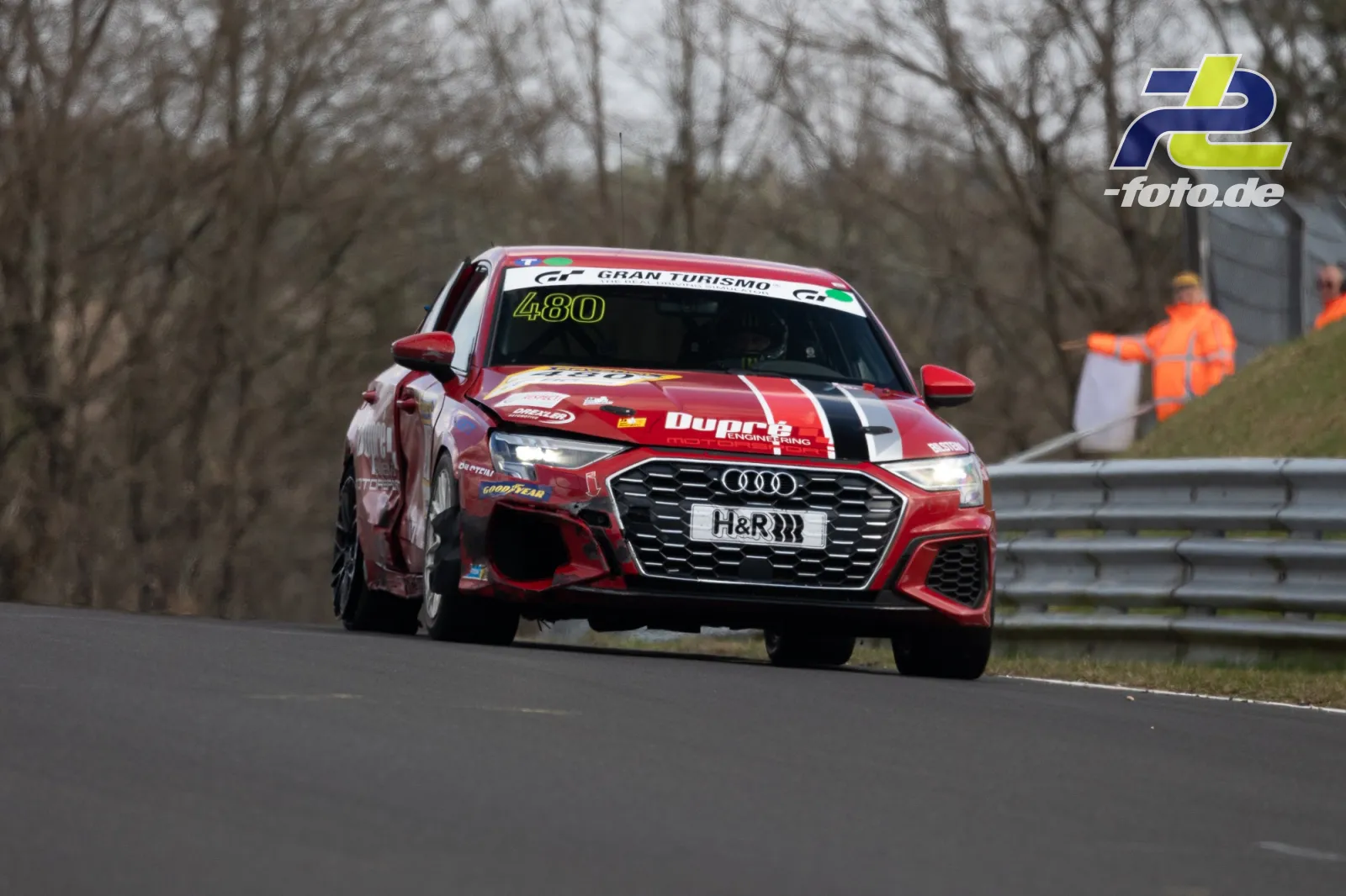 Audi Nummer 480 in rot-weißer Lackierung auf der Nordschleife beim NLS Rennen, Streckenposten im Hintergrund.