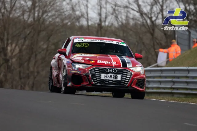 Audi Nummer 480 in rot-weißer Lackierung auf der Nordschleife beim NLS Rennen, Streckenposten im Hintergrund.