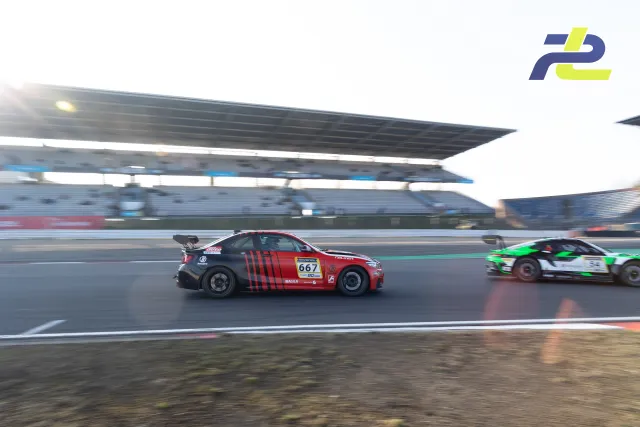 BMW M240i Racing Cup  667 in rot-schwarz auf der Geraden vor der Haupttribüne des Nürburgrings, dahinter ein weiteres Fahrzeug.