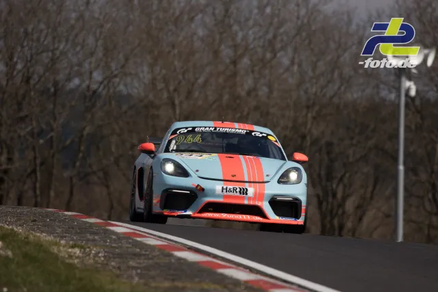 Porsche Cayman GT4 in hellblau-orangeroter Lackierung auf der Nordschleife des Nürburgrings während des Rennens.