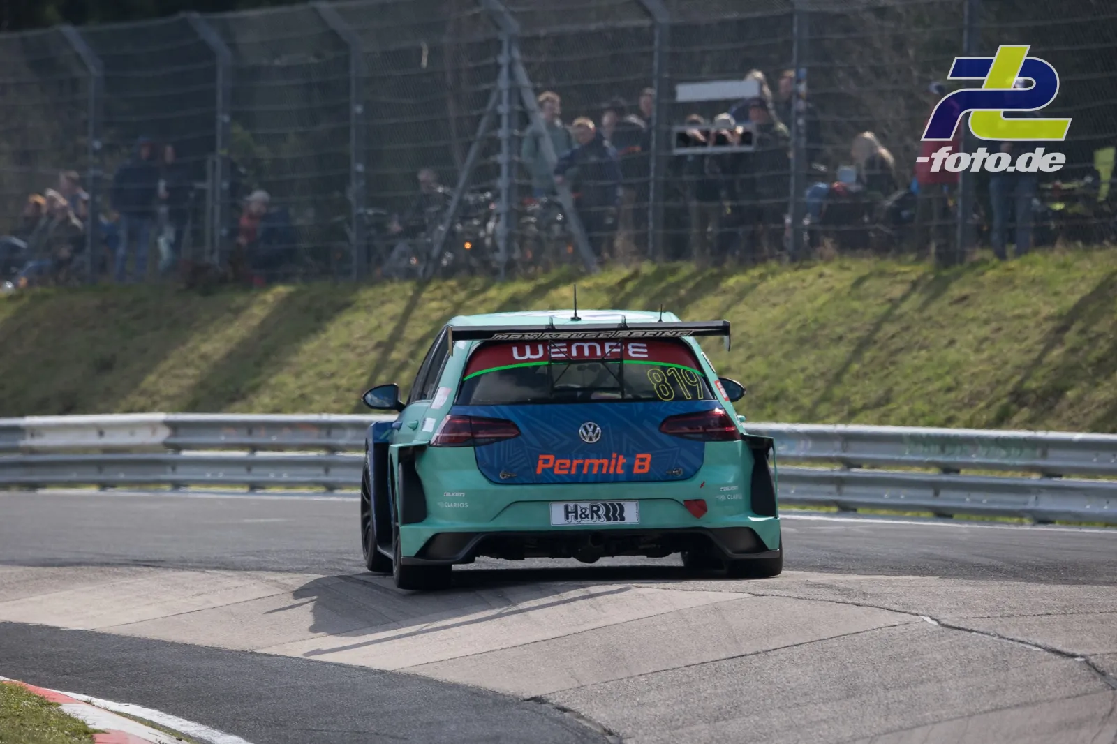 VW TCR #819 in türkis-blauer Lackierung von hinten auf dem Nürburgring, Zuschauer hinter Fangzaun.