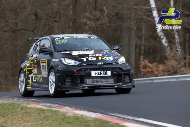 Toyota GR Yaris #109 in Kurve auf der Nürburgring Nordschleife beim NLS Rennen, schwarz-gelbe Lackierung mit weißen Felgen.