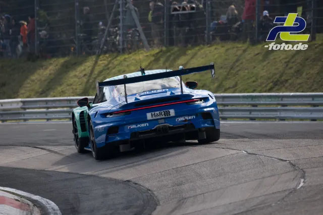 Porsche 911 GT3 R in blau-türkiser Lackierung von hinten in einer Kurve auf dem Nürburgring, Zuschauer am Streckenrand.