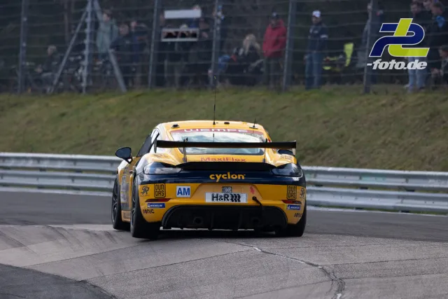 Porsche 718 Cayman GT4 in Gelb-Schwarz aus Heckperspektive auf dem Nürburgring bei NLS-Rennen, Zuschauer im Hintergrund.
