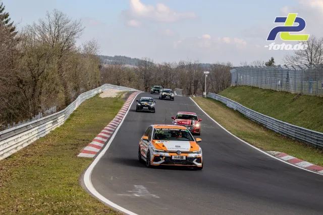 Rennfahrzeuge auf der Nordschleife während des Rennens, angeführt von einem weiß-orangen VW Polo.
