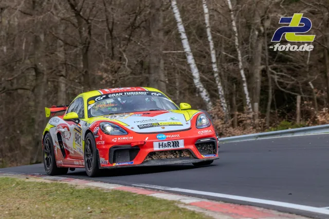 Porsche 718 Cayman GT4 in rot-gelber Lackierung während des Rennens auf der Nordschleife, Waldpassage im Hintergrund