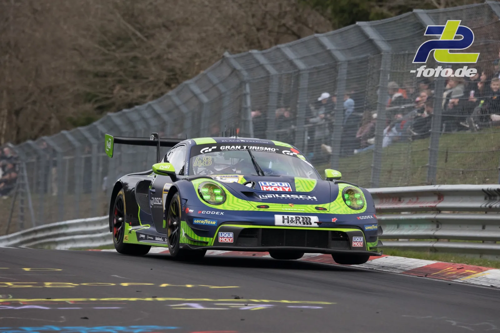 Porsche 911 GT3 R #48 in dunkelblau-neongrüner Lackierung fährt über rot-weiße Randsteine auf der Nürburgring-Nordschleife beim NLS-Rennen.