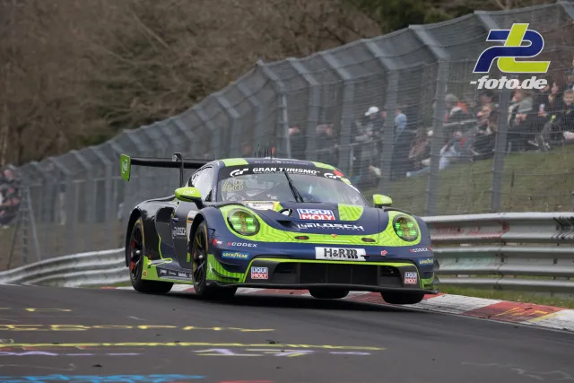 Porsche 911 GT3 R #48 in dunkelblau-neongrüner Lackierung fährt über rot-weiße Randsteine auf der Nürburgring-Nordschleife beim NLS-Rennen.