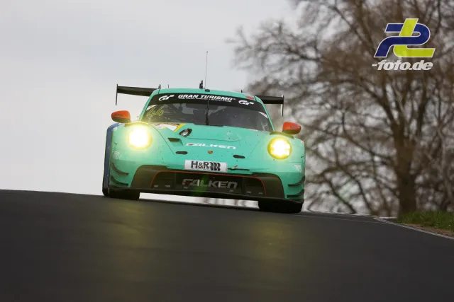 Porsche 911 GT3 R in türkiser Falken-Lackierung über Kuppe fliegend auf der Nordschleife, Scheinwerfer eingeschaltet.