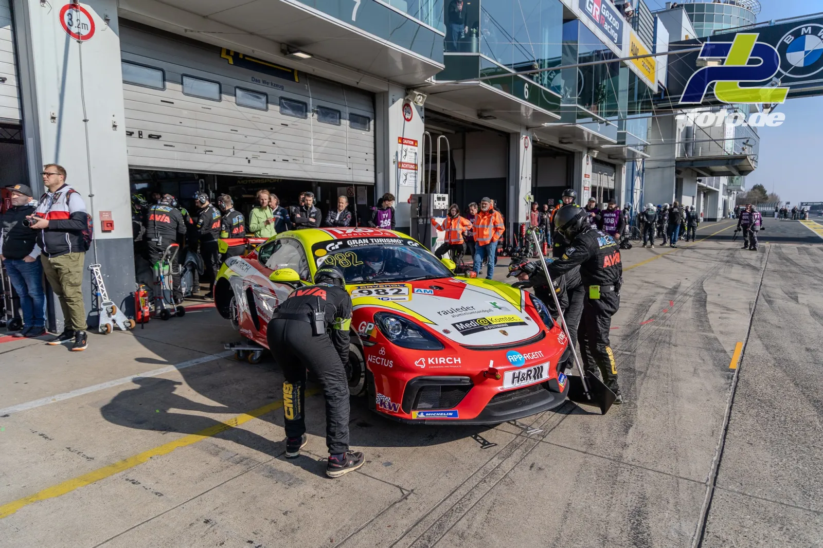 Porsche 718 Cayman GT4 Clubsport #982 wird in der Boxengasse vom Team vorbereitet, Mechaniker arbeiten am Fahrzeug.
