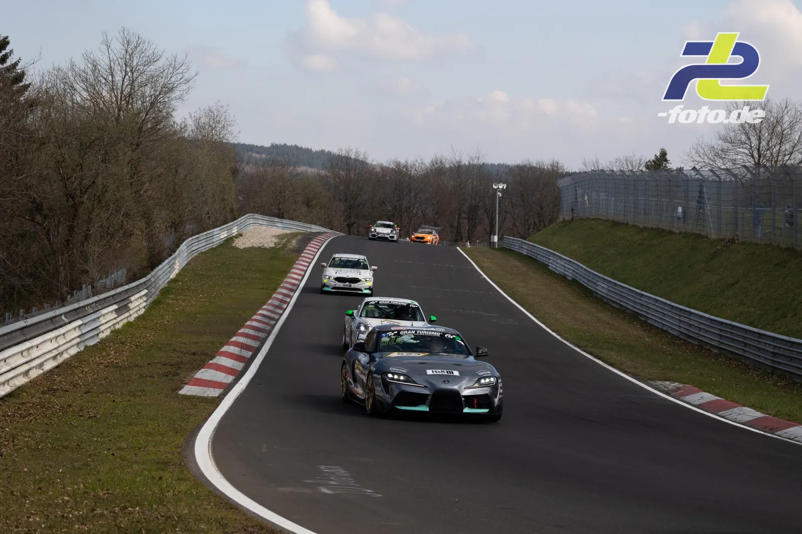 Fünf Rennwagen fahren hintereinander durch eine Kurve am Nürburgring, angeführt von einem Toyota GR Supra in schwarz mit türkisfarbenen Akzenten.