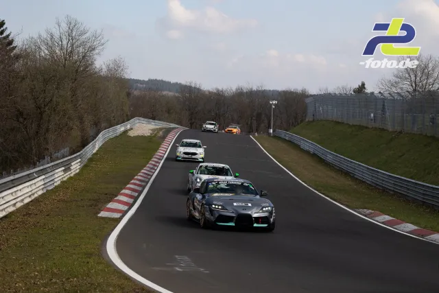 Fünf Rennwagen fahren hintereinander durch eine Kurve am Nürburgring, angeführt von einem Toyota GR Supra in schwarz mit türkisfarbenen Akzenten.