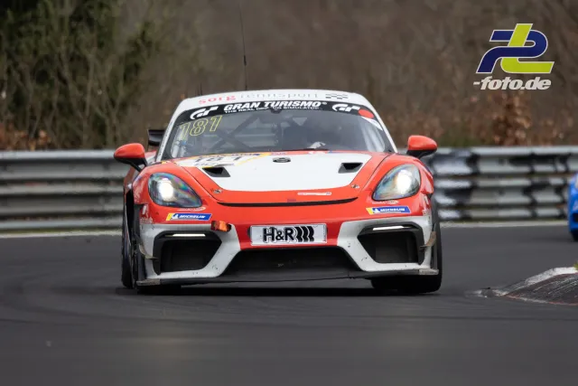 Porsche 718 Cayman GT4 Clubsport #187 in orange-weißer Lackierung beim NLS-Rennen am Nürburgring in Frontansicht auf der Strecke.