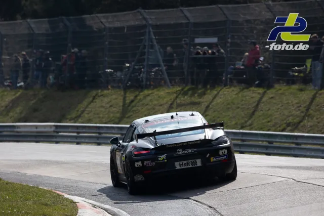 Porsche 718 Cayman GT4 in schwarz-weißer Lackierung während des Rennens am Nürburgring, Heckansicht mit Zuschauern im Hintergrund